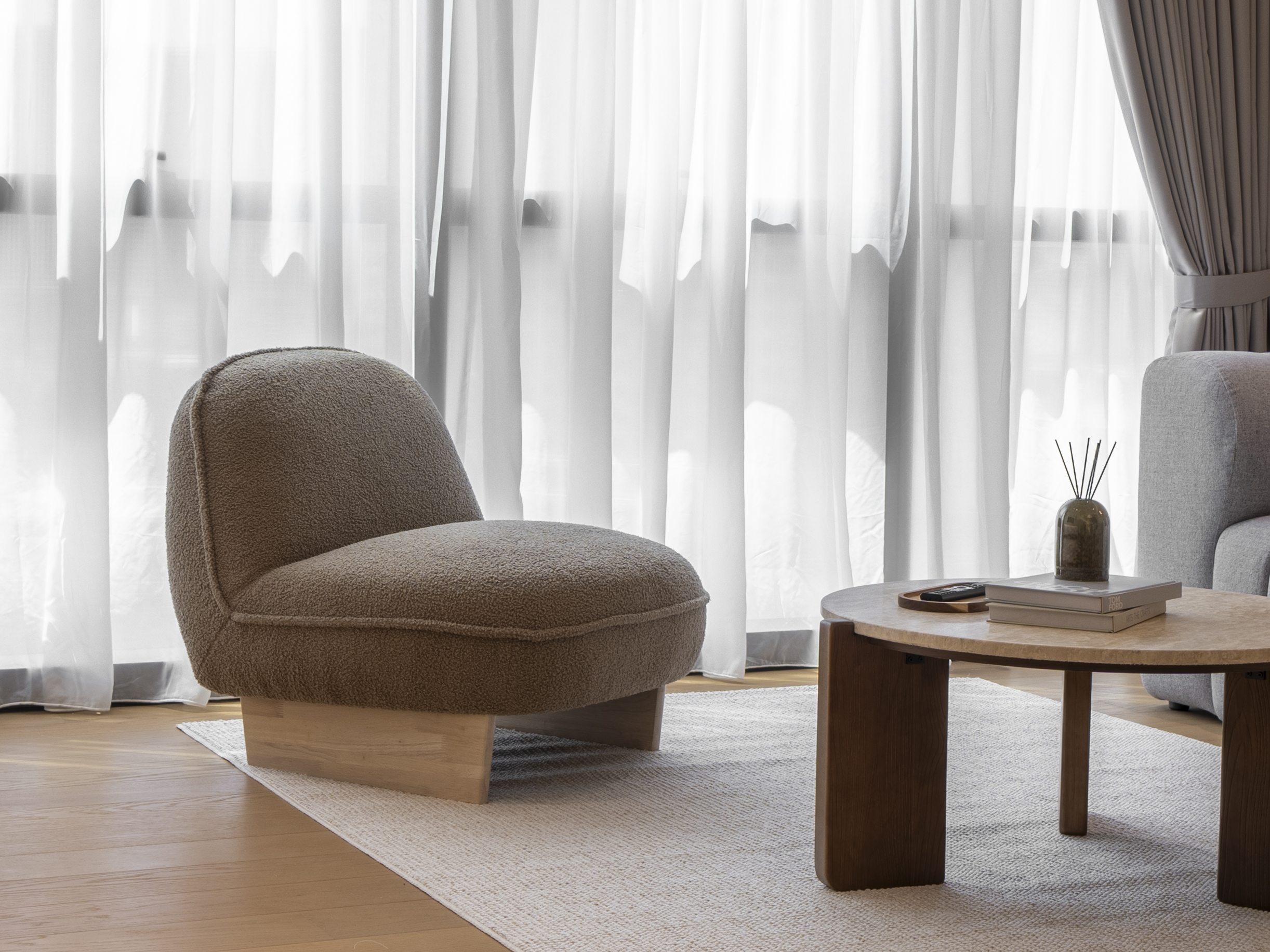 Curved lounge chair beside sheer curtains and a timber coffee table at TRX Residence, Unit 02